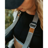 A close up of a grey camera strap attached to a camera with a brown leather square that has a "LP" etched into it for Lizzie Peirce.