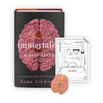 A black book with a pink brain in the middle and a person atop that. The text reads "Immortality; A love story". Next to the book is a black and white bookplate with illustrations of medical equipment. At the bottom corner of the bookplate is a pin shaped like a brain in light pink and gold. From Noble Blood.  