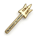 A golden pin shaped like a trident with the words "The Newest Olympian" etched in black down the staff. 