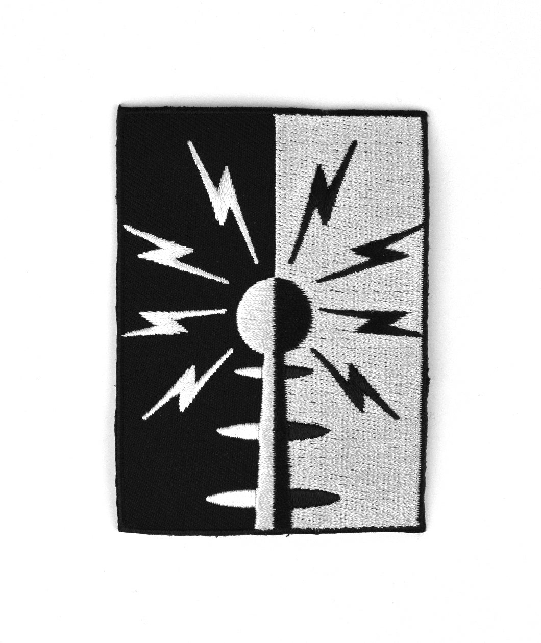 A vertical rectangular patch half black and half white. There is a circle in the center on top of a cone with three ovals going down the cone. Eight lightning bolts surround the circle. Half of image is white and half is black - from Tesladyne