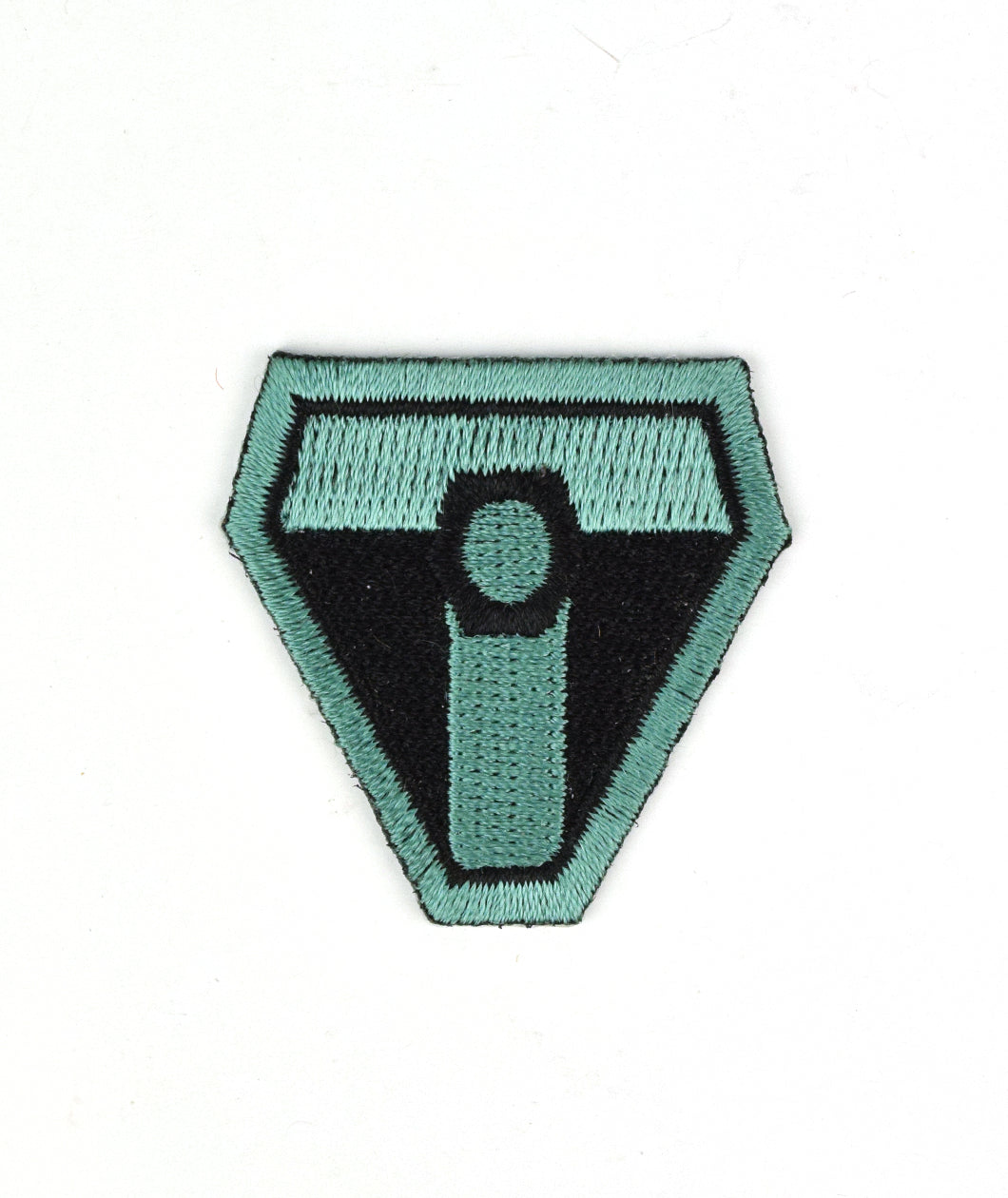 A black upside down triangular patch with a thick teal outline and squared off edges. A teal “T” is in the center with a black octagon in the center and a teal circle in the center of that - from Tesladyne