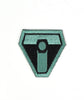 A black upside down triangular patch with a thick teal outline and squared off edges. A teal “T” is in the center with a black octagon in the center and a teal circle in the center of that - from Tesladyne