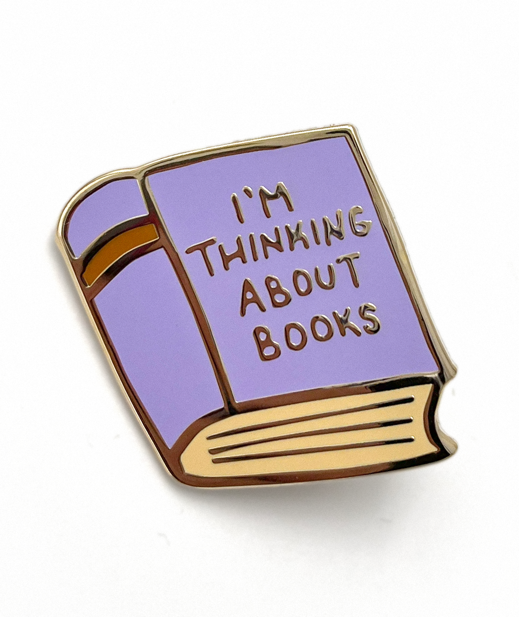 A gold and purple pin shaped like a book. The cover of the book says "I'm thinking about books". From Ariel Bissett.
