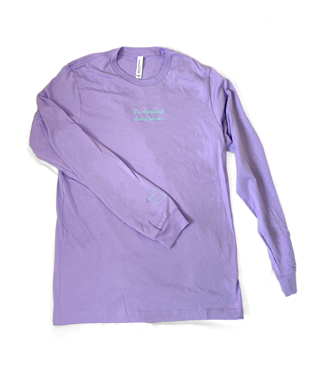 A lavender long sleeve shirt with mint writing on the front center and a small mint outline of a book on the left sleeve - by Ariel Bissett