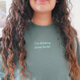 Close-up of the phrase "I'm thinking about books" written in mint on an alpine green sweatshirt worn by Ariel Bissett