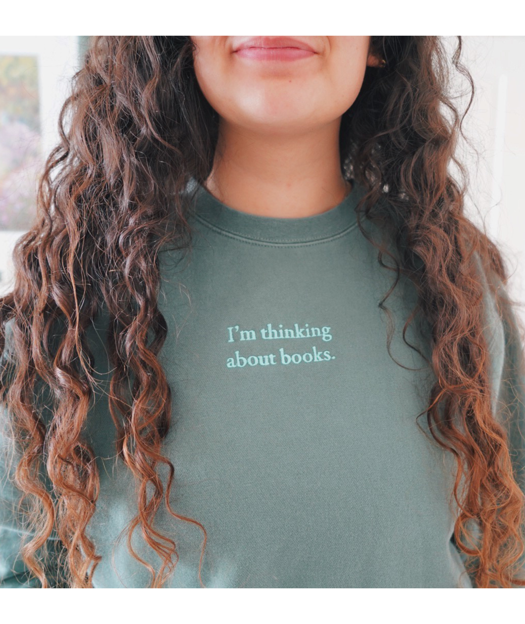 Close-up of the phrase "I'm thinking about books" written in mint on an alpine green sweatshirt worn by Ariel Bissett