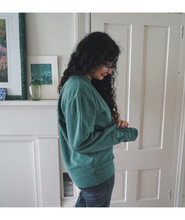 Ariel Bissett holding the left sleeve of her alpine green sweatshirt which has a small mint green outline of a book on it.