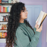 Ariel Bissett reading while wearing an alpine green sweatshirt with a mint green outline of a book on the sleeve.
