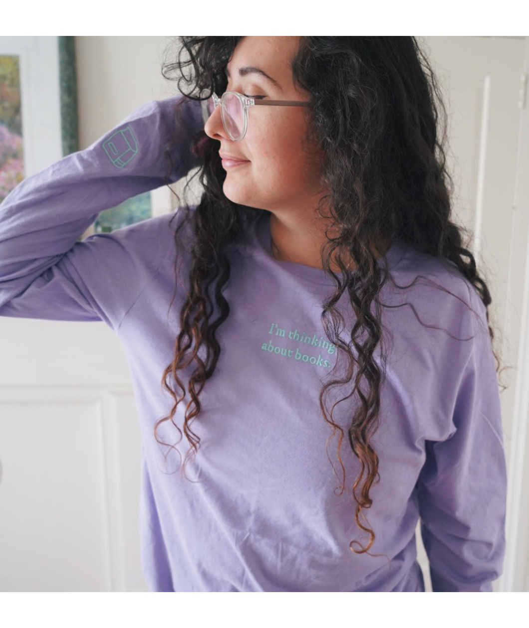 Ariel Bissett modeling a lavender long sleeve shirt with the phrase "I'm thinking about books" in mint on the front center. It has a small mint outline of a book on the left sleeve. 