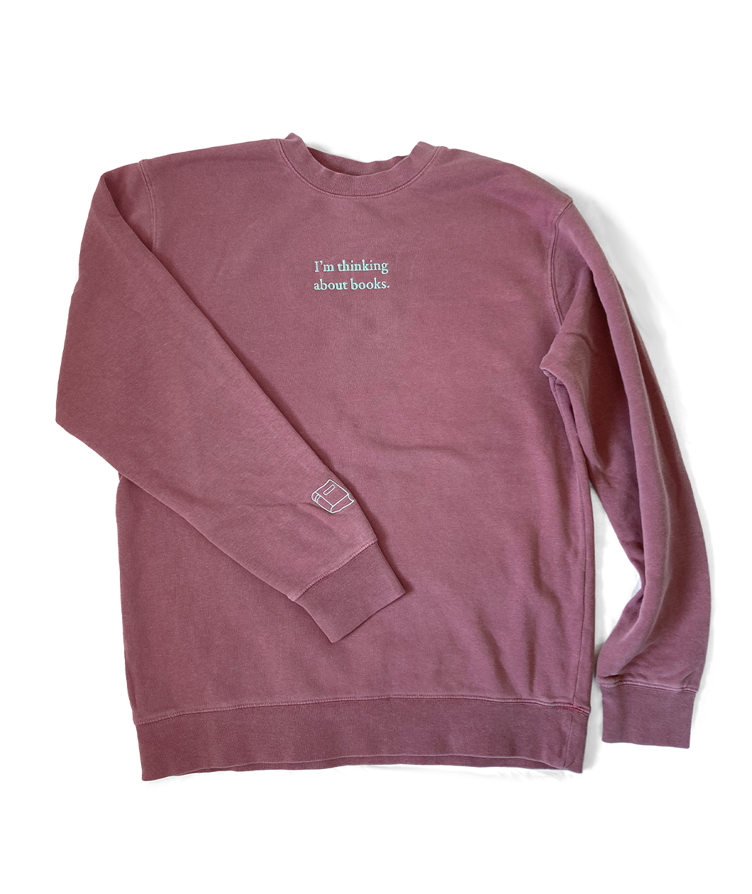 A dusty rose sweatshirt with mint green writing on the front center and a small mint green outline of a book on the left sleeve - by Ariel Bissett