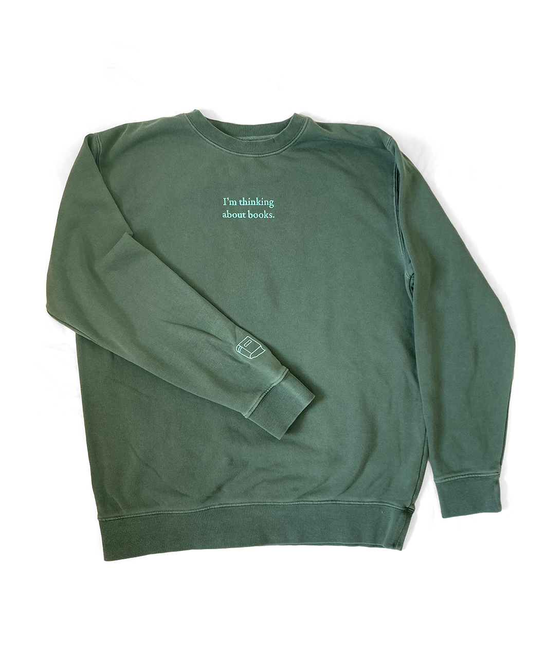 An alpine green sweatshirt with mint green writing on the front center and a small mint green outline of a book on the left sleeve - by Ariel Bissett