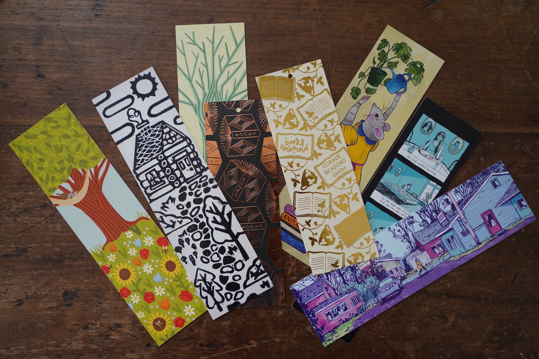 8 different illustrated, colorful bookmarks from the Books Unbound subscription laying overlapping on a table. 