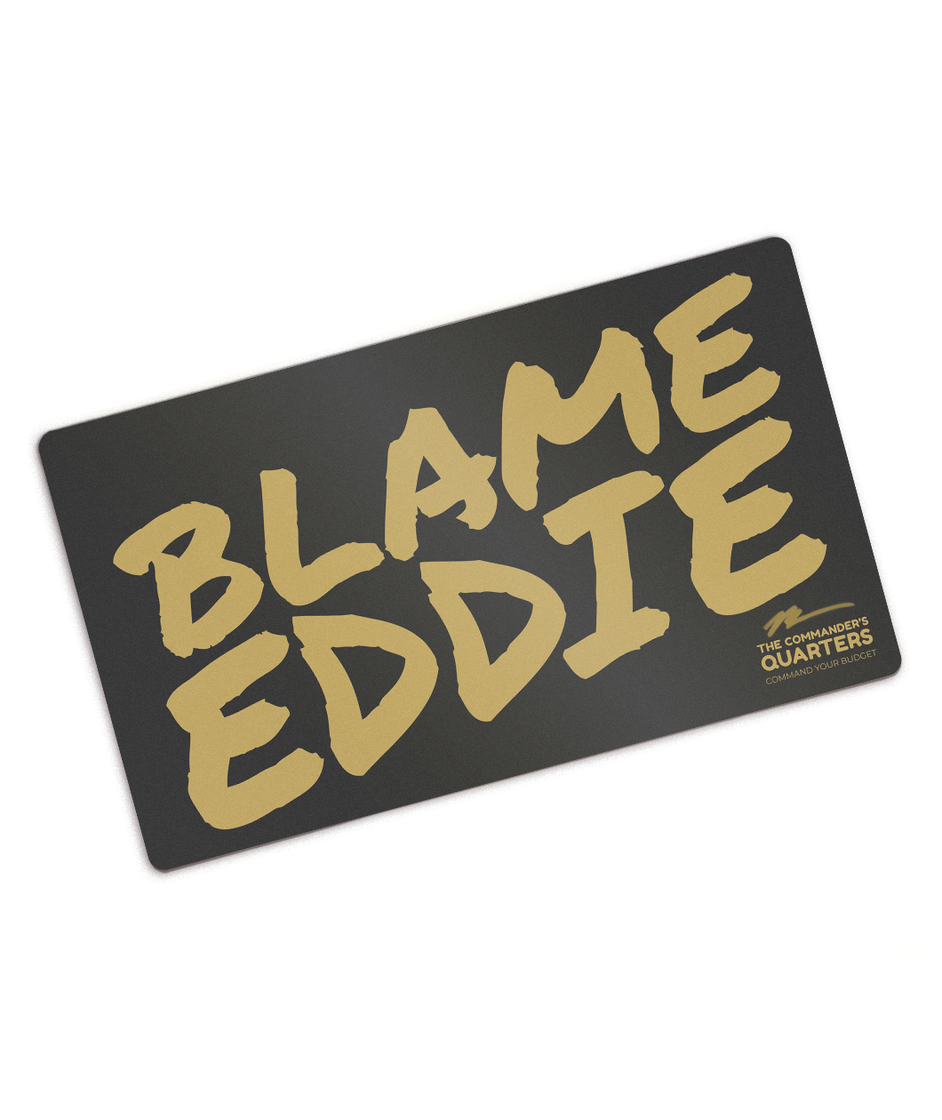 Black rectangular playmat with curved corners. “Blame Eddie” is in gold font resembling handwriting. “The commander’s quarters” is in the bottom right corner in gold sans serif font with a gold signature above it - from The Commander’s Quarters