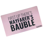 A pink rectangular playmat with curved edges. “First Up There’s Wayfarer’s Bauble” is in black sans serif font in varying weights in the center. “The Commander’s Quarter’s” is in the bottom right of the playmat - from the Commander’s Quarters