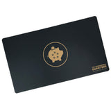 A black rectangular playmat with curved corners. In the center is a gold outlined circle. A gold piggy bank is in the center with a coin being inserted. On the pig are five black outlined circles. “The Commander’s Quarters” is in the bottom right in gold sans serif font - from The Commaner’s Quarters