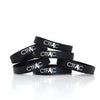 A pile of black silicone wristbands with white text and cancer ribbon - by Charles Trippy