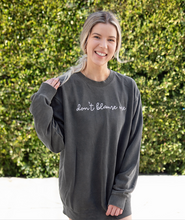 Meghan Rienks modeling a gray crewneck sweatshirt with “don’t blame me” across chest in white cursive font - from Don’t Blame Me