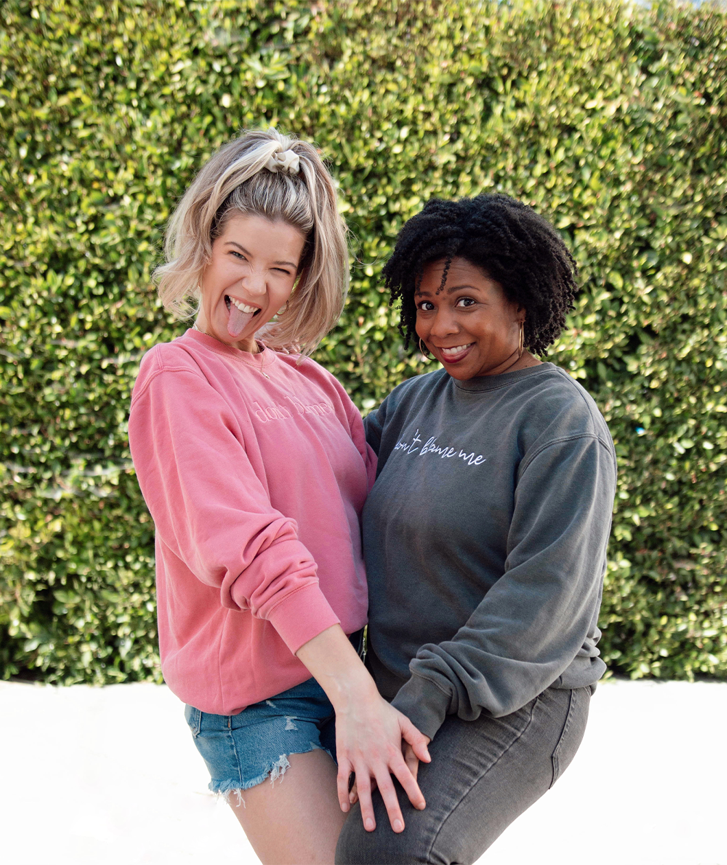 Meghan Rienks modeling a pink crewneck sweatshirt with “don’t blame me” across the chest in pink serif font and Melisa Monts modeling a gray crewneck sweatshirt with “don’t blame me” across chest in white cursive font - from Don’t Blame Me