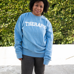 Melisa Monts modeling a light blue crewneck sweater with “Therapy” in white with a gray outline arched across the chest - from Don’t Blame Me