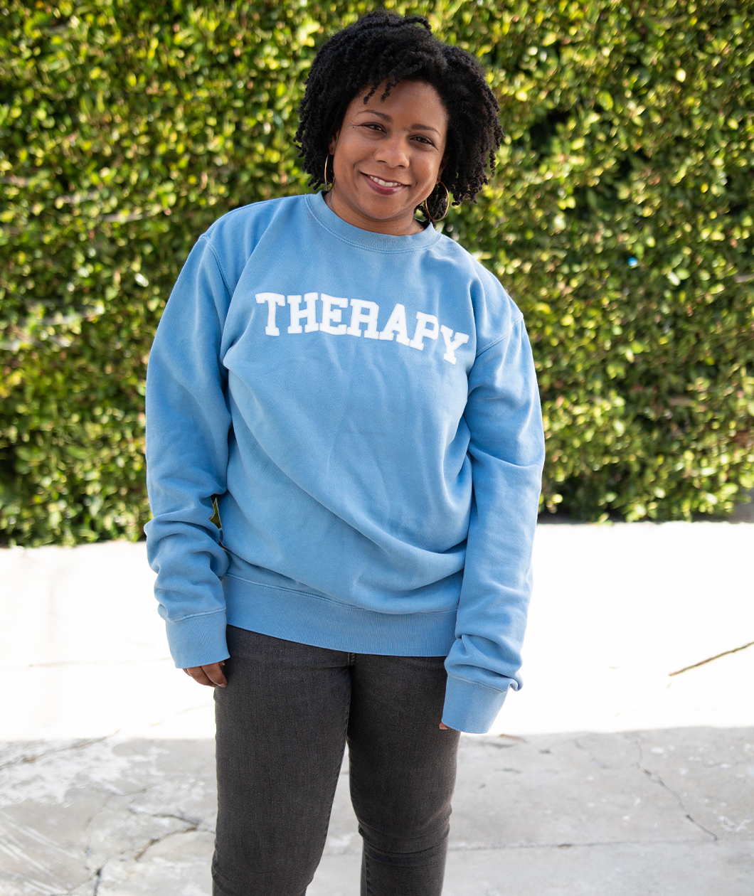 Melisa Monts modeling a light blue crewneck sweater with “Therapy” in white with a gray outline arched across the chest - from Don’t Blame Me