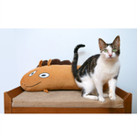 The Jacob Horse plushie is an oblong light brown horse with a crooked smile and eyes on one side of its body. It has little legs, ears and a mane and tail. In this picture it is sitting behind a cat.