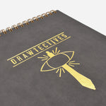 A close-up on a gold drawing of a sword and an eye below the word "Drawtectives"- by Drawfee