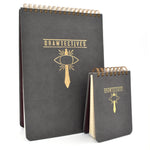 One large and one small black spiral notepad with gold writing and drawing - by Drawfee