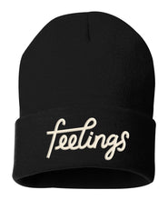 Black beanie with “feelings” in white cursive font cross the front. The “f” and “l” connect to each other - from Iz Harris