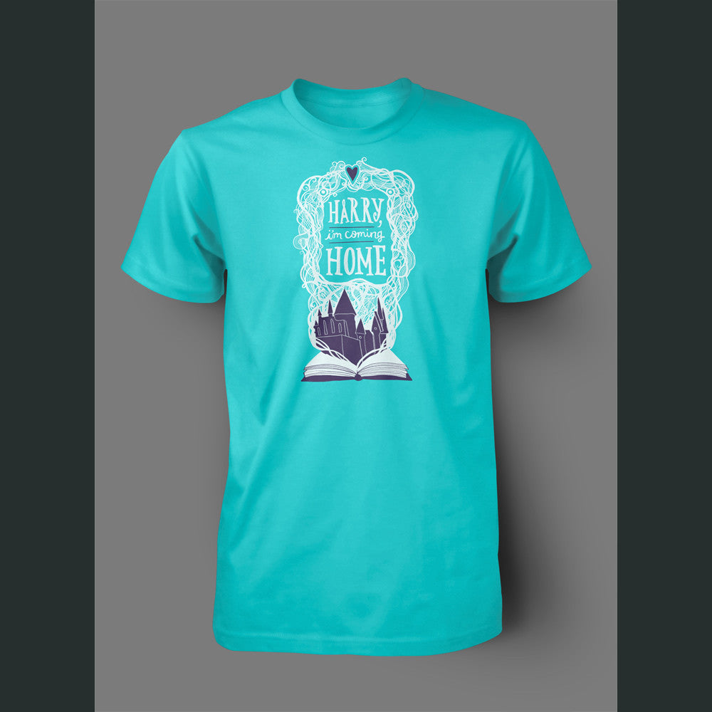A light teal shirt with an open book with a white outline drawing with purple fill of Hogwarts. White intertwined lined surround “Harry I’m Coming Home” in white font. A purple heart is atop - from Lauren Fairweather