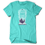 A light teal shirt with an open book with a white outline drawing with purple fill of Hogwarts. White intertwined lined surround “Harry I’m Coming Home” in white font. A purple heart is atop - from Lauren Fairweather