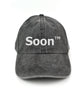 A gray hat with “Soon” in white sans serif font across the front. Following the word is “TM” at the top right of the word in white sans serif font - from JoCo Cruise