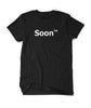 A black shirt with “Soon” in white sans serif font across the front. Following the word is “TM” at the top right of the word in white sans serif font - from JoCo Cruise