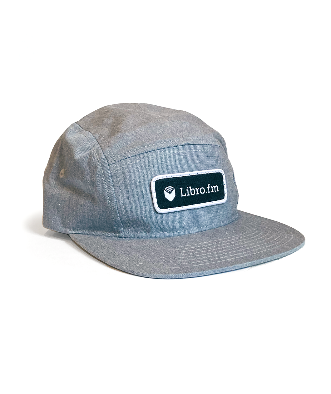 A light gray hat with a black patch and white outline on the front. On the patch, a white open book with three arched white lines above it is followed my “Libro.fm” in white sans serif font - from Libro.fm
