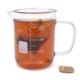 A glass beaker with a mug handle full of brown tea and a tea bag. On the side of the mug is the NileRed logo and a square that says 400mL and shows a scale of 350mL.