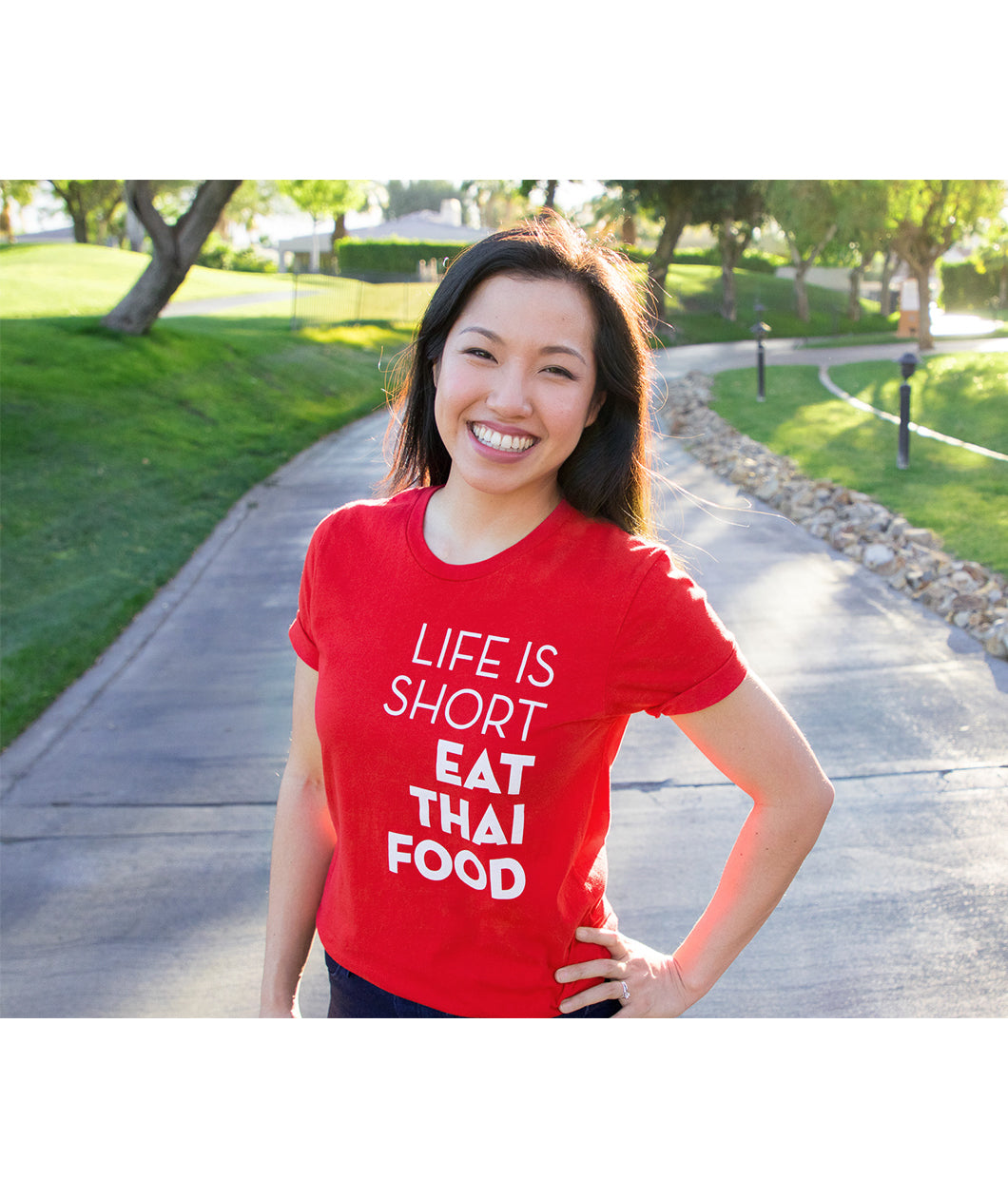 A bright red t-shirt with the words "Life Is Short Eat Thai Food" written down the right side worn by Pailin from Hot Thai Kitchen. 