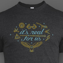 Grey shirt with “It’s real for us” in light blue cursive font surrounded by line drawings of various Harry Potter objects in gold with light blue highlights. Light blue stars in various sizes also surround text - from Lauren Fairweather
