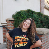 A girl modeling a blue shirt with “Confident & Kind” in half yellow and half orange organic fond. The words are surrounded by various flowers and stars - from Sierra Schultzzie