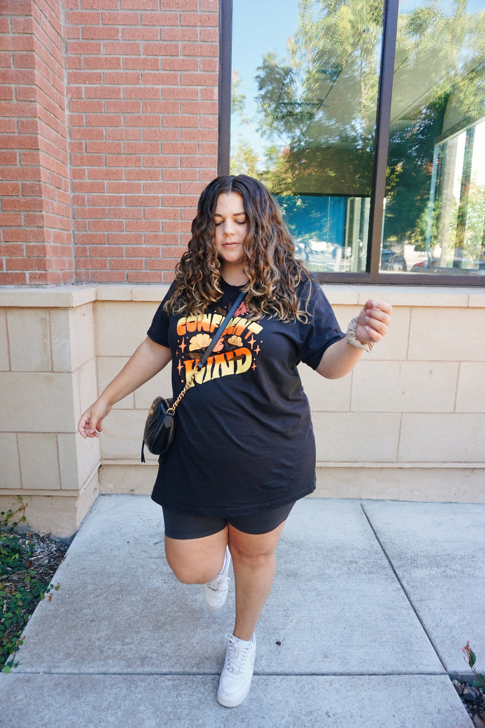 A girl modeling a blue shirt with “Confident & Kind” in half yellow and half orange organic fond. The words are surrounded by various flowers and stars - from Sierra Schultzzie
