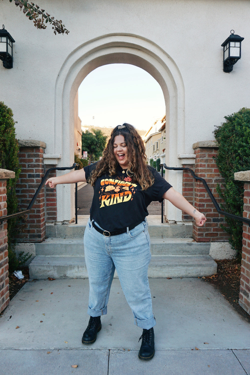 A girl modeling a blue shirt with “Confident & Kind” in half yellow and half orange organic fond. The words are surrounded by various flowers and stars - from Sierra Schultzzie