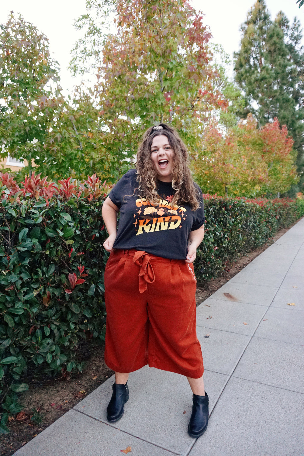 A girl modeling a blue shirt with “Confident & Kind” in half yellow and half orange organic fond. The words are surrounded by various flowers and stars - from Sierra Schultzzie