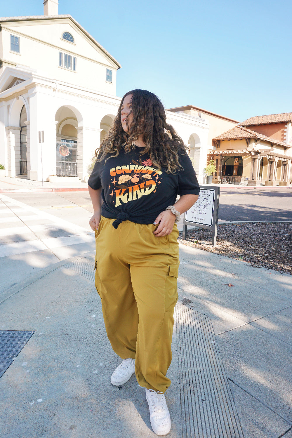 A girl modeling a blue shirt with “Confident & Kind” in half yellow and half orange organic fond. The words are surrounded by various flowers and stars - from Sierra Schultzzie