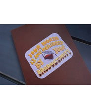 A rectangular purple sticker with curved edges on a brown notebook. “Your worth is not measured by your productivity” is in yellow organic font with white highlights. A vector drawn coffee pot is between “by” and “your” and is filling up the word” productivity” with coffee - from Sierra Schultzzie