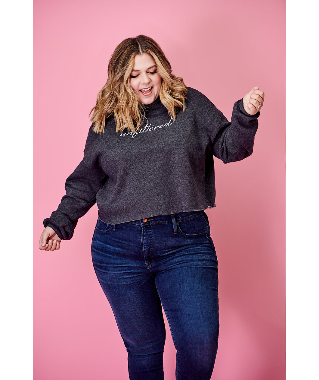 A woman modeling a dark gray crop top hoodie with “unfiltered” in white cursive font across the chest - from Sierra Schultzzie