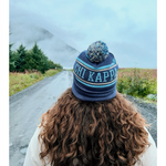 A person with their back to the camera with flowing brown hair wearing a blue knit beanie that reads "Chi Kappa". From Sierra Schultzzie.