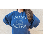 A person wearing an oversized blue crewneck that reads "Chi Kappa; Social Club" across the front with a picture of two pinkys intertwined. From Sierra Schultzzie.
