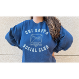 A person wearing an oversized blue crewneck that reads "Chi Kappa; Social Club" across the front with a picture of two pinkys intertwined. From Sierra Schultzzie.