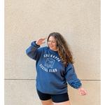 A person wearing an oversized blue crewneck that reads "Chi Kappa; Social Club" across the front with a picture of two pinkys intertwined. From Sierra Schultzzie.