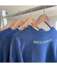 A set of blue crewnecks hanging on hangers with "Where all are welcome" written across the top of the backs. From Sierra Schultzzie.