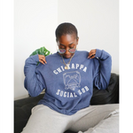 A person wearing an oversized blue crewneck that reads "Chi Kappa; Social Club" across the front with a picture of two pinkys intertwined. From Sierra Schultzzie.