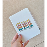 A white journal that has the words "Chi Kappa" written in four different colors on the front. Below that it says "Social Club Est. 2018". The journal is being held by a hand. From Sierra Schultzzie.